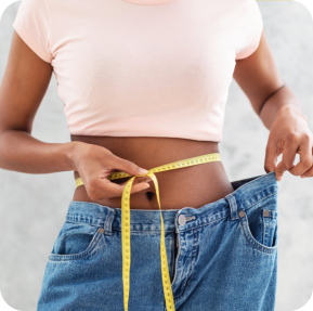 Closeup of black woman in old big jeans measuring her waist with tape